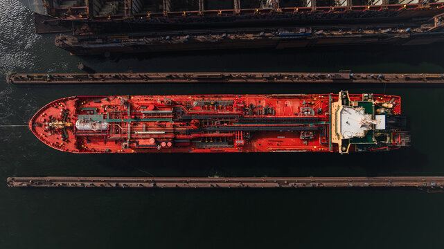 Red LPG tanker escorted by tugboats on calm sea waters, maritime transport, industrial shipping, logistics, and port operations concept.
