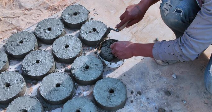 close up of a worker's hands using a trowel to cast circular concrete spacers in molds.