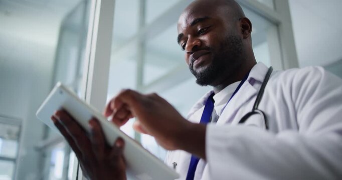 Medical, low angle or man in hospital with tablet, research or patient diagnosis in online consulting. Healthcare, space or black doctor with technology, telehealth or case report for treatment plan.