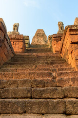 Fototapeta premium Low-angle view of ancient stone steps ascending toward the weathered central tower of Pre Rup temple in Cambodia, flanked by eroded guardian statues. The scene is bathed in warm late afternoon light