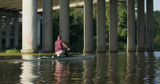 A rower confidently steers a canoe during training. A man and a woman canoeist confidently paddle along the river.