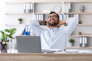 Satisfied middle aged caucasian guy with beard in glasses resting from work at laptop in office or living room interior. Successful business and deal during covid-19 outbreak. Take a break, enjoy job