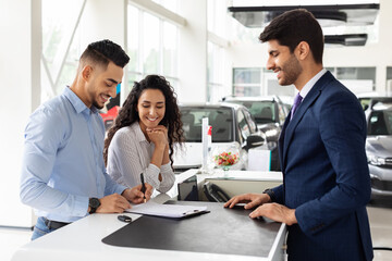 Wealthy arab family buying new car in showroom, standing by counter with handsome man sales...