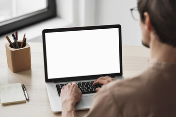 Young man using laptop computer with blank empty mockup screen. Business man working at home. Freelance, student lifestyle, e-learning, shopping online, web site, technology concept