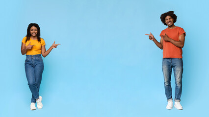 Beautiful millennnial black man and woman in casual outfits showing copy space between them on blue...