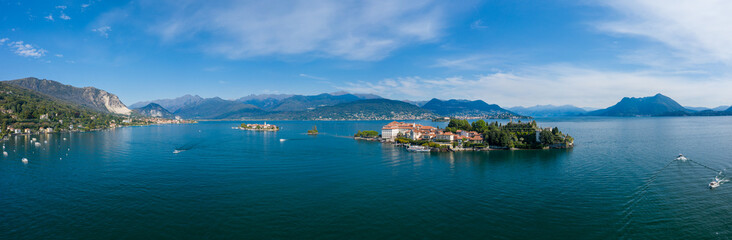 Fototapeta premium Wide aerial panorama of the Borromean Islands on Lake Maggiore, with terracotta rooftops, lush greenery, and deep blue water set against a backdrop of alpine mountains under a clear sky in northern