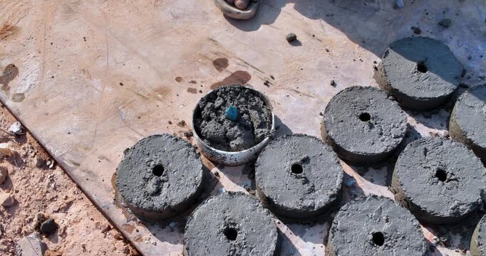 close up of a worker's hands using a trowel to cast circular concrete spacers in molds.