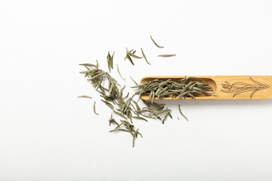 High-quality dried green tea leaves in a wooden scoop on a white background
