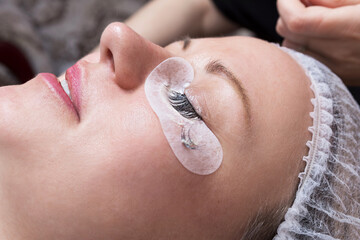 Applying eyelash extensions to a happy female client in a beauty salon