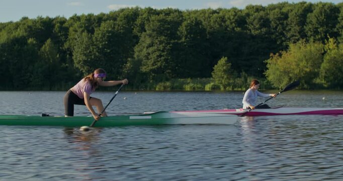 Female rowers are paddling hard during training. Two women in a canoe and a kayak paddle along the river, actively working on rowing technique.