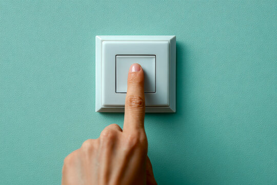 Person pressing a white electrical switch on a textured teal wall to turn on or off lighting in a modern interior setting with focus on hand and switch mechanism