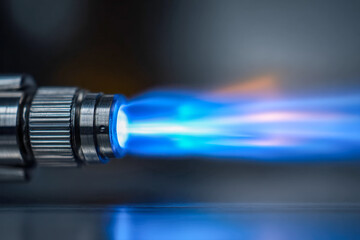 High-intensity blue flame from a metal blow torch igniting with focused heat for precision tasks in industrial and craft applications on a reflective surface