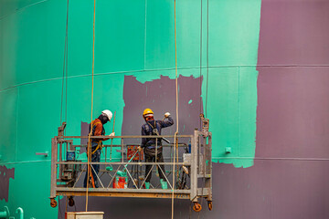 The male worker takes the cable car holding an industrial painting brush used for shell plate tank oil surface surface green