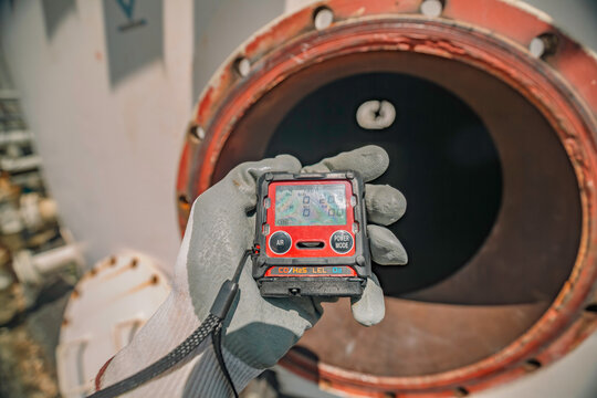 Worker hand holding gas detector inspection safety gas testing at front manhole