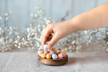 Child hand picking easter chocolate Multi-Colored eggs from wooden bowl with gypsophila on background.