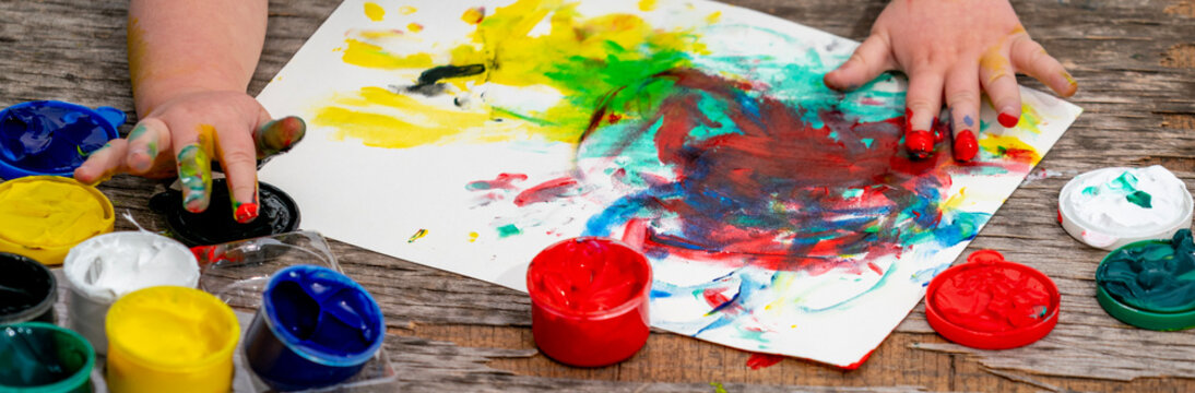 Child creating abstract artwork with finger painting, enjoying sensory play and creative exploration of colorful paints.