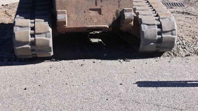 Heavy machine moves on worksite, shaping ground with tracks gravel during works day.