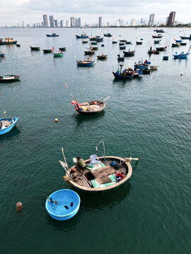 Aerial view of coracle boats bobbing in deep blue waters, contrasting with the distant skyline of modern buildings, Da Nang, Da Nang, Vietnam.