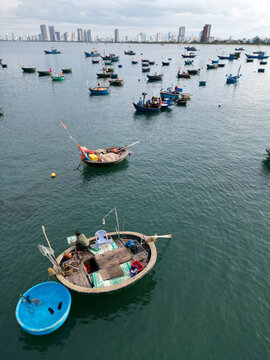 Aerial view of a vibrant flotilla of round fishing boats bobs on the tranquil, dark turquoise waters near Da Nang's skyline, each vessel a tiny world of labor and life., Da Nang, Da Nang, Vietnam.