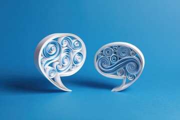 Close-up of two paper-crafted quote marks with swirling interior design, blue background