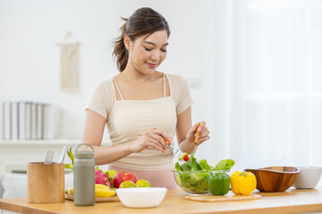Smiling asian woman preparing fresh healthy vegetable salad kitchen showing happiness while cooking organic meal for wellness diet lifestyle home table with bowl green lettuce pepper and food