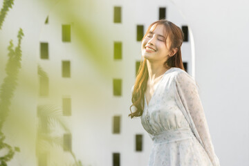 Portrait of happy young beautiful asian woman smiling with cheerful face in white dress enjoying relaxing summer holiday at green garden backyard