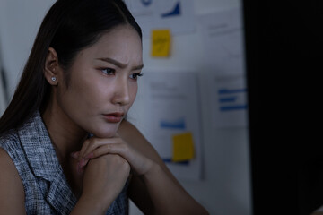 Concentrated serious asian woman working late night shift with computer looking anxious and tired at office desk analyzing business chart financial report