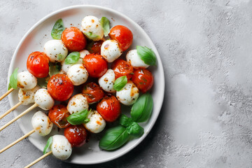 Colorful skewers of cherry tomatoes and mozzarella balls garnished with fresh basil leaves on a round plate, showcasing a vibrant and appetizing presentation of a delicious appetizer