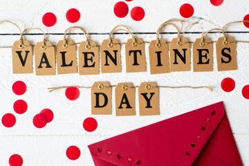 Valentines day greeting card, red envelop with wooden letters on white wooden background with confetti.