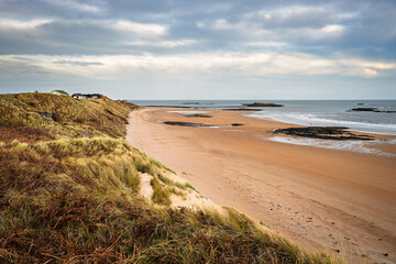 Beach Huts on Embleton Links look over Embleton Bay, which is a long stretch of sand overlooked by the dramatic ruins of Dunstanburgh Castle located on the North Sea coast in the National Landscape