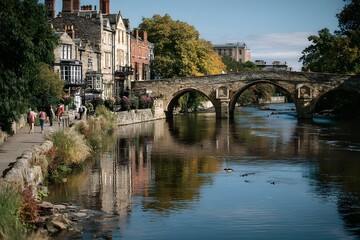 Fototapeta premium Solidity wide shot of a stone bridge over calm river with pedestrians and buildings backdrop