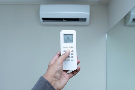 A hand holds an air conditioner remote control, setting the temperature to 25&deg;C for energy efficient level. Climate control, home comfort, and energy saving concept.
