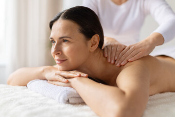 Fototapeta premium Smiling woman relaxing after spa massage, lying on treatment bed. Concept of wellness, body therapy, self care, and positive healthy lifestyle indoors