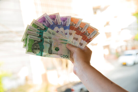 Close-up of a hand holding Colombian peso bills outdoors, representing money, income, savings, the economy, cash payments, and financial success in Colombia. Minimum wage