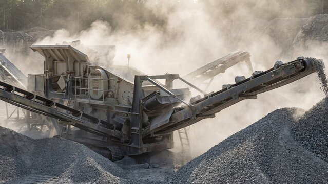 Industrial stone crusher machine processing rock into gravel at a quarry with dust. Heavy construction equipment for mining and aggregate production