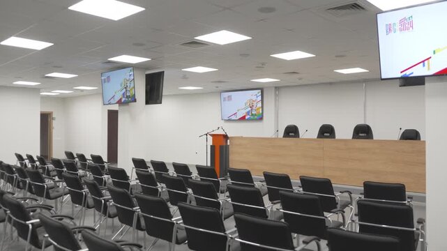 Conference hall equipped with speaker podium and wall mounted televisions. Technical setup supports presentations with communication
