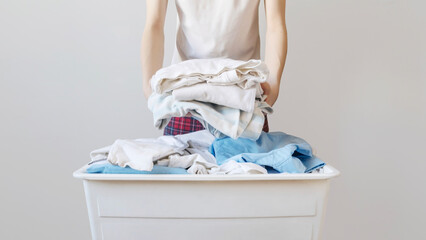 Person Holding a Large Stack of Folded Laundry Over a White Plastic Basket. Modern Concept of Home Organization, Sustainable Laundry Habits, and Minimalist Domestic Life for 2026 Housekeeping Branding