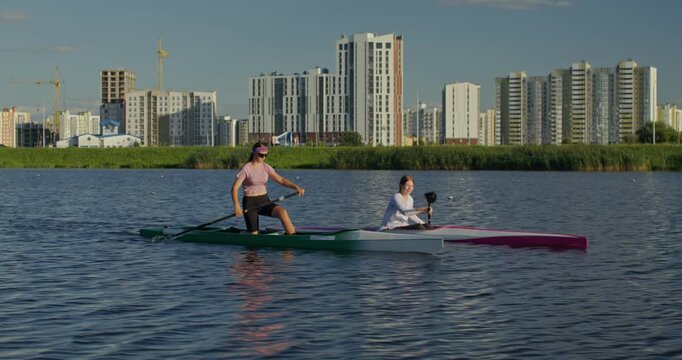 Girls in a kayak and canoe paddle side by side down the river during training. Two women in a canoe and a kayak paddle along the river, actively working on rowing technique.