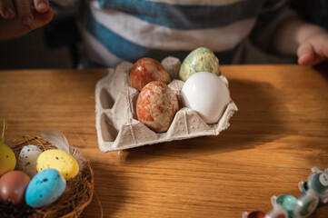 A close-up of a tray of Easter eggs on a table, a child colors them independently in preparation for the Easter holiday