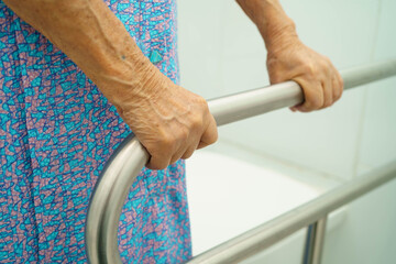 Asian elderly woman patient use toilet support rail in bathroom.