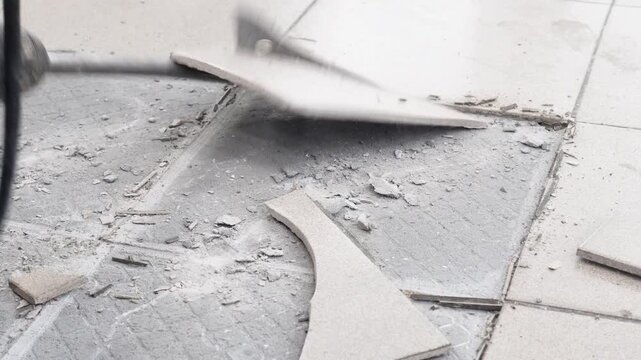 Removing a concrete floor with a hand hammer. Concrete rubble on the construction site of a house. Destruction of old tiles. Male construction removes the old tile from the floor with a hammer drill.
