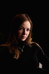 A woman with long brown hair poses subtly against a dark backdrop, exuding confidence and allure. Her gaze holds intrigue, inviting onlookers to delve into her story.