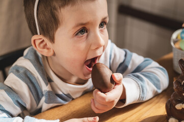 A boy dressed as a bunny eats a chocolate egg in the kitchen celebrating Easter.