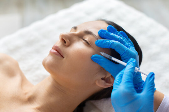 Closeup of young beautiful woman undergoing professional aesthetic facial procedure with syringe, calm expression, clean clinic setting highlighting modern skincare and beauty treatment