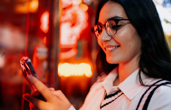 Young woman looking into phone screen with hand on face, showing disappointed or concerned expression, taking selfie in dimly lit entrance hallway.