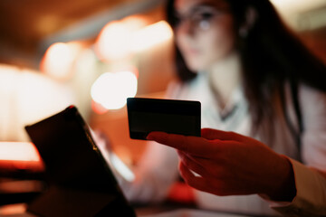 Close-up of a woman holding a credit card while using a tablet, illustrating a digital payment scenario and the intersection of fintech, identity, and secure online transactions.