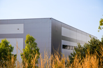 Modern industrial warehouse roof with white corrugated metal sheet against blue sky.Exterior of modern gray industrial building or logistics center with green trees