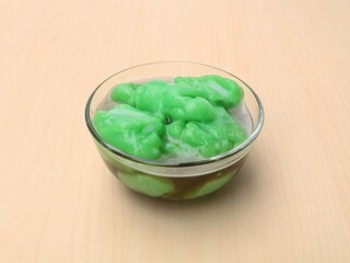 Indonesian green rice pudding with palm sugar syrup (Bubur sumsum pandan) served in a glass bowl with wooden table background. High angle view 