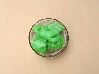 Indonesian green rice pudding with palm sugar syrup (Bubur sumsum pandan) served in a glass bowl with wooden table background. Flat lay 