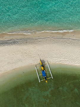 Aerial view of a traditional outrigger boat resting on the pristine white sands where the turquoise sea meets the shore, Mambajao, Camiguin, Philippines.